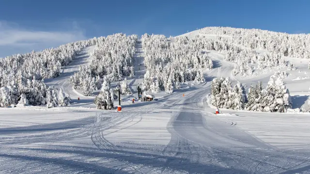 Vue sur les pistes enneigées de la station des Angles, bordées de forêts de sapins sous un ciel bleu dégagé.