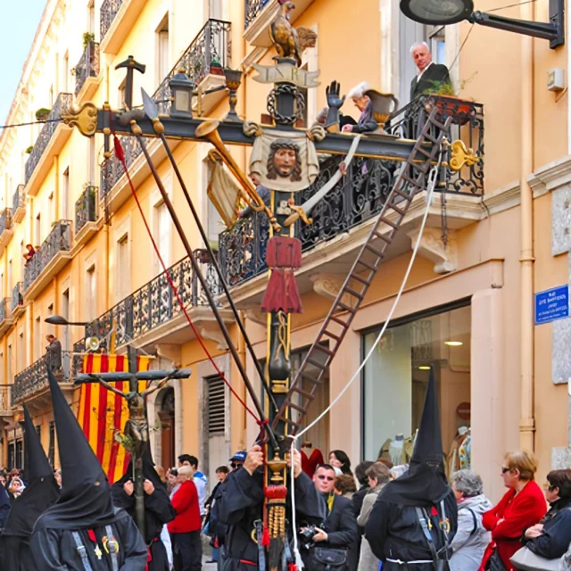 Pénitents en habits noirs et cagoules pointues portant la grande croix de la Sanch ornée de symboles de la Passion du Christ, lors de la procession à Perpignan.