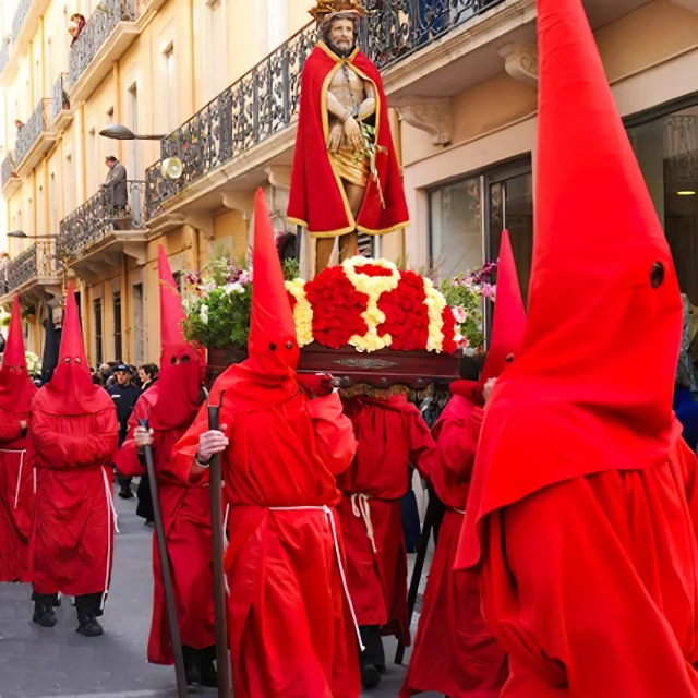 Pénitents en habits rouges et cagoules pointues portant une statue religieuse de Jésus couronné d’épines et drapé d’un manteau rouge, lors de la Procession de la Sanch à Perpignan.
