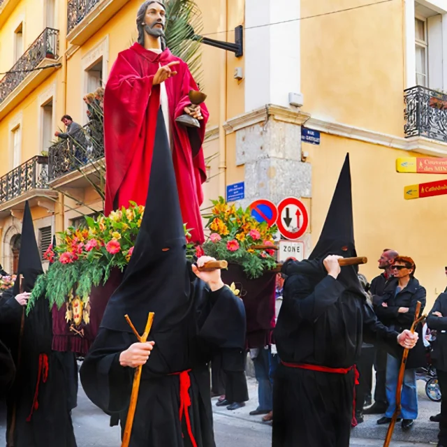Pénitents en habit noir et cagoule pointue portant une statue religieuse de Jésus en robe rouge lors de la Procession de la Sanch à Perpignan, dans une rue du centre historique.