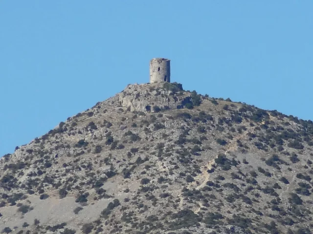 La Torre del Far, tour de guet médiévale en pierre située au sommet d’une colline rocailleuse à Tautavel, sous un ciel bleu clair.