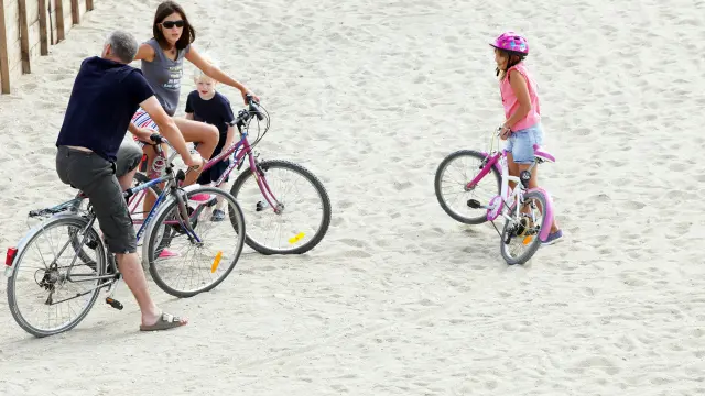 Famille avec des vélos arrêtée sur une zone sablonneuse en bord de mer.