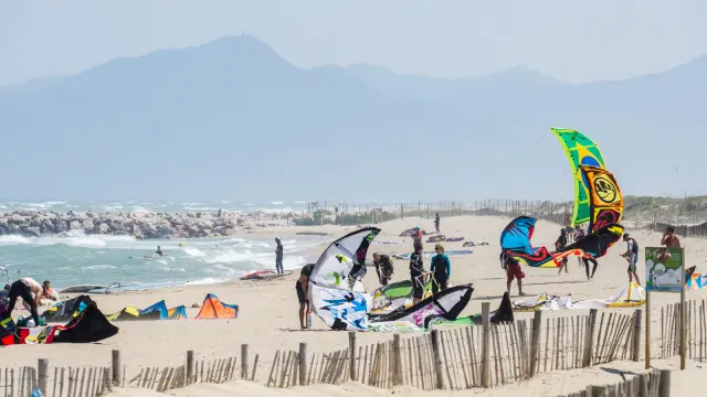 Plage ventée avec pratiquants installant leurs ailes de kitesurf près du rivage.
