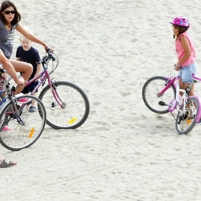 Famille avec des vélos arrêtée sur une zone sablonneuse en bord de mer.