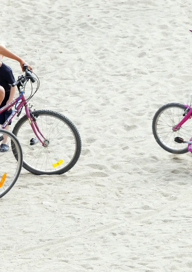 Famille avec des vélos arrêtée sur une zone sablonneuse en bord de mer.