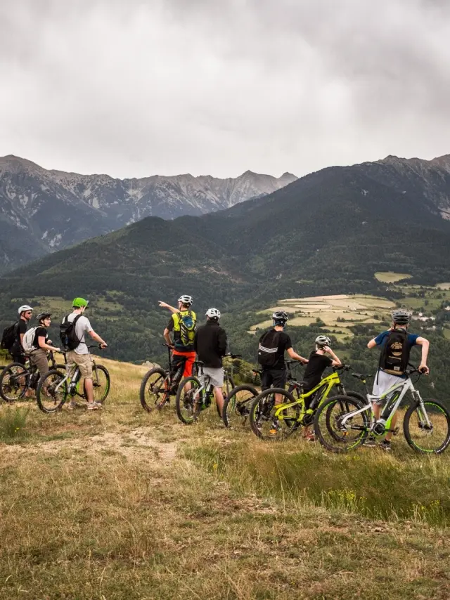 Groupe de cyclistes à VTT électrique arrêtés sur un plateau herbeux, observant un vaste panorama de montagnes et de vallées.