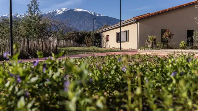Gîte Alter & Go à Marquixanes, bâtiment de plain-pied entouré de verdure avec le massif du Canigó enneigé en arrière-plan.