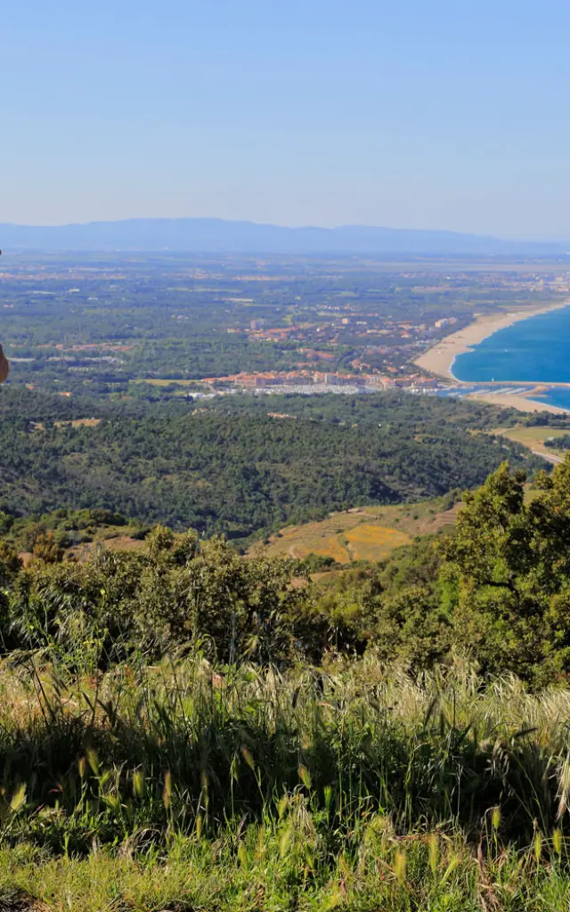 Deux personnes équipées de sacs à dos observent un large panorama côtier depuis un sentier en hauteur sous un ciel dégagé.