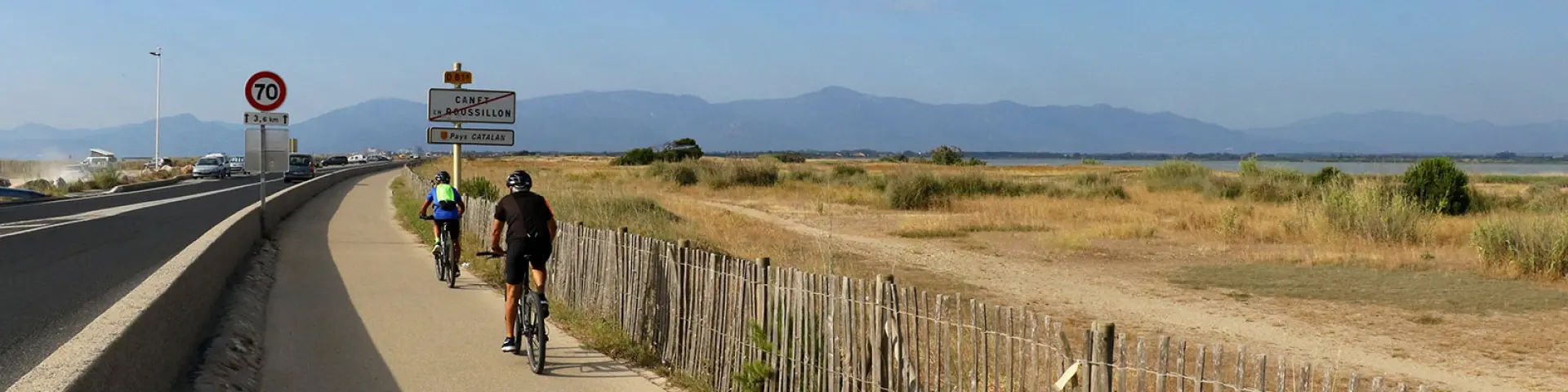 Cyclistes roulant sur une piste aménagée longeant une route et une zone naturelle.