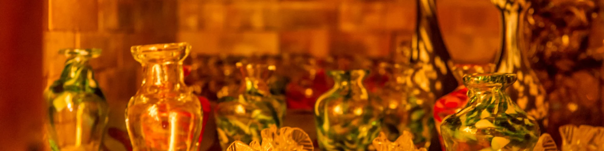 Petits vases et objets décoratifs en verre soufflé posés sur une étagère éclairée d’une lumière chaude.