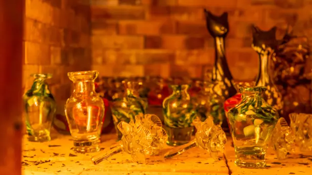 Petits vases et objets décoratifs en verre soufflé posés sur une étagère éclairée d’une lumière chaude.