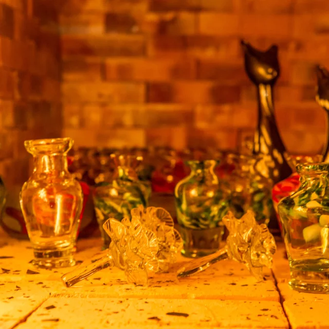 Petits vases et objets décoratifs en verre soufflé posés sur une étagère éclairée d’une lumière chaude.
