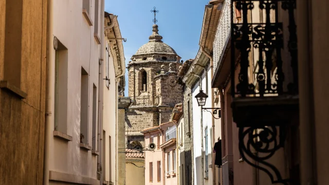 Rue étroite bordée de maisons, avec un clocher en pierre visible au bout de la perspective.