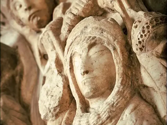 Sculpture romane en pierre représentant plusieurs visages et figures sculptées en relief, photographiée en gros plan.