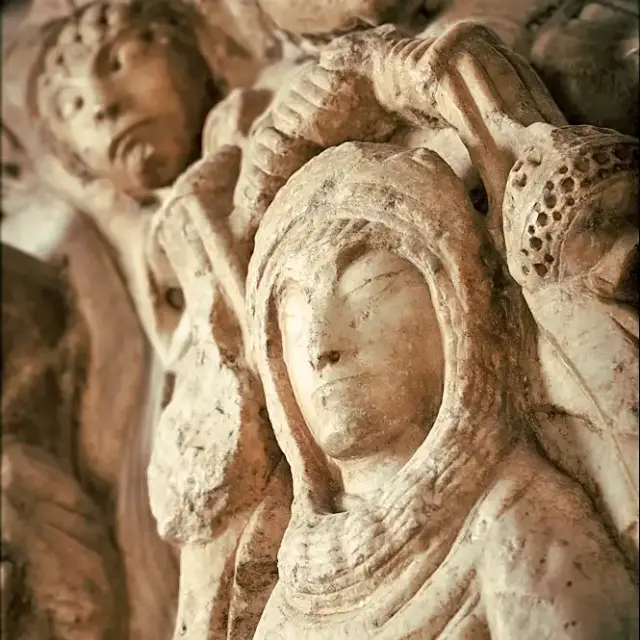Sculpture romane en pierre représentant plusieurs visages et figures sculptées en relief, photographiée en gros plan.