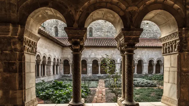 Vue du jardin intérieur du cloître à travers des arcades sculptées en pierre ornées de chapiteaux décorés.