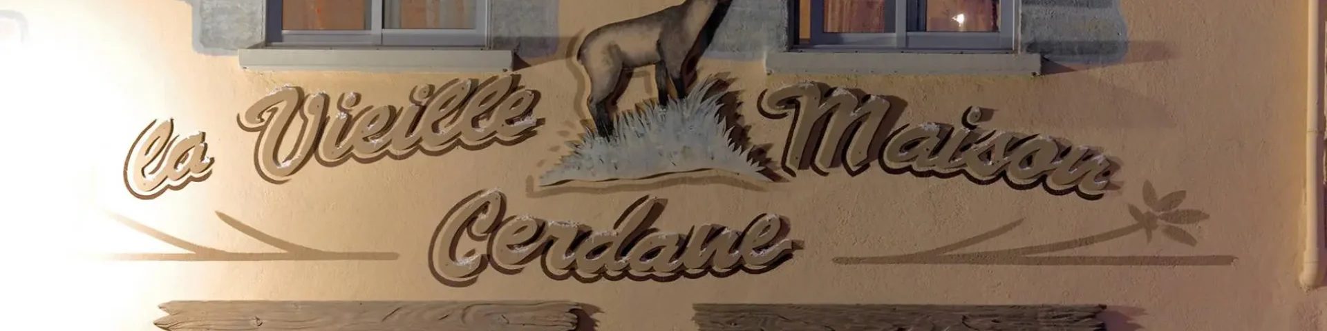 Façade d’un bâtiment avec deux fenêtres et une enseigne peinte représentant un animal et du texte décoratif.