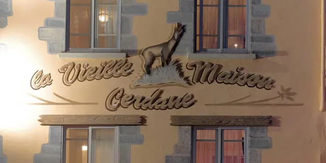 Façade d’un bâtiment avec deux fenêtres et une enseigne peinte représentant un animal et du texte décoratif.