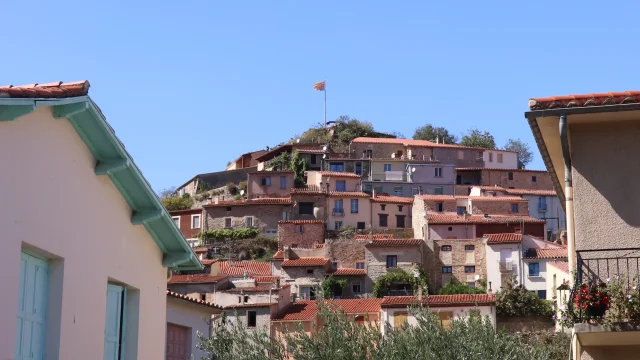 Maisons aux toits rouges de Ria-Sirach sur une colline, vues depuis un quartier résidentiel au premier plan, sous un ciel bleu dégagé.