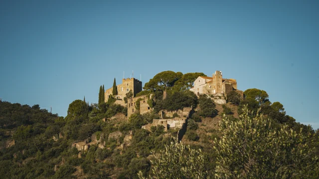 Village perché avec bâtiments anciens en pierre, entouré de végétation méditerranéenne et situé sur une colline.