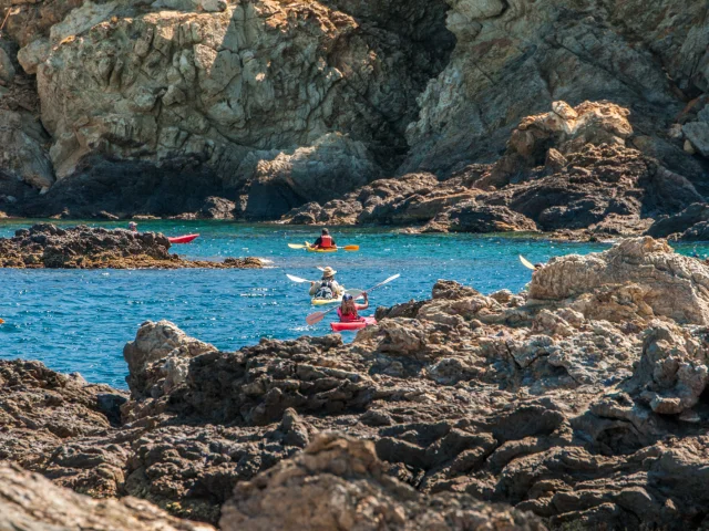 Kayaks naviguant entre des rochers côtiers dans une eau turquoise, au pied de falaises rocheuses.