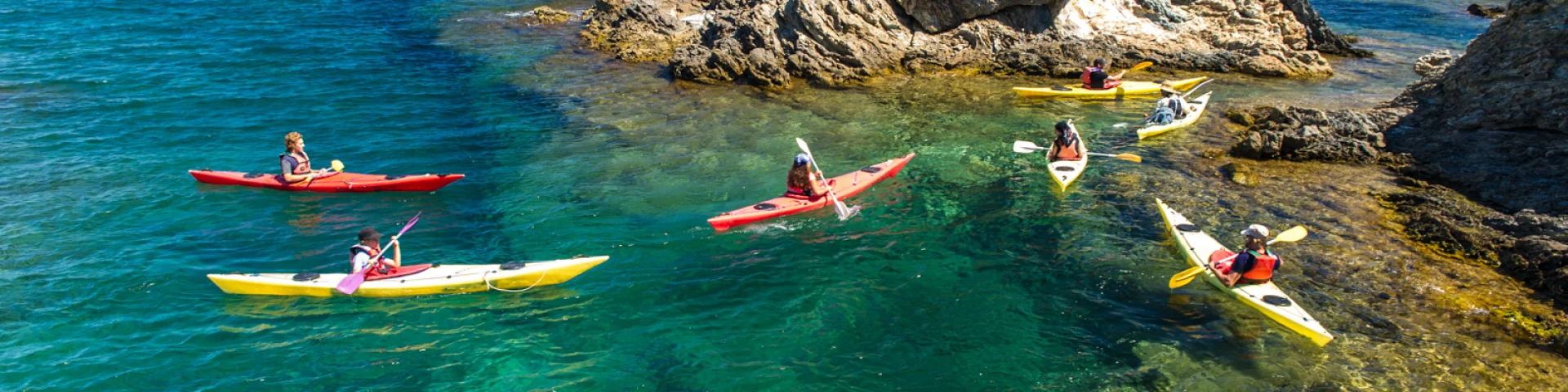 Groupe de personnes en kayak sur une eau turquoise, près de rochers côtiers.