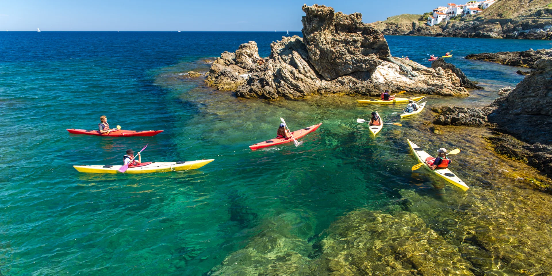 Groupe de personnes en kayak sur une eau turquoise, près de rochers côtiers.
