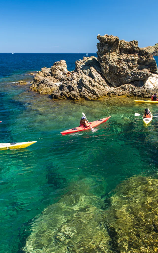 Groupe de personnes en kayak sur une eau turquoise, près de rochers côtiers.