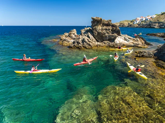 Groupe de personnes en kayak sur une eau turquoise, près de rochers côtiers.