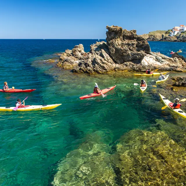 Groupe de personnes en kayak sur une eau turquoise, près de rochers côtiers.