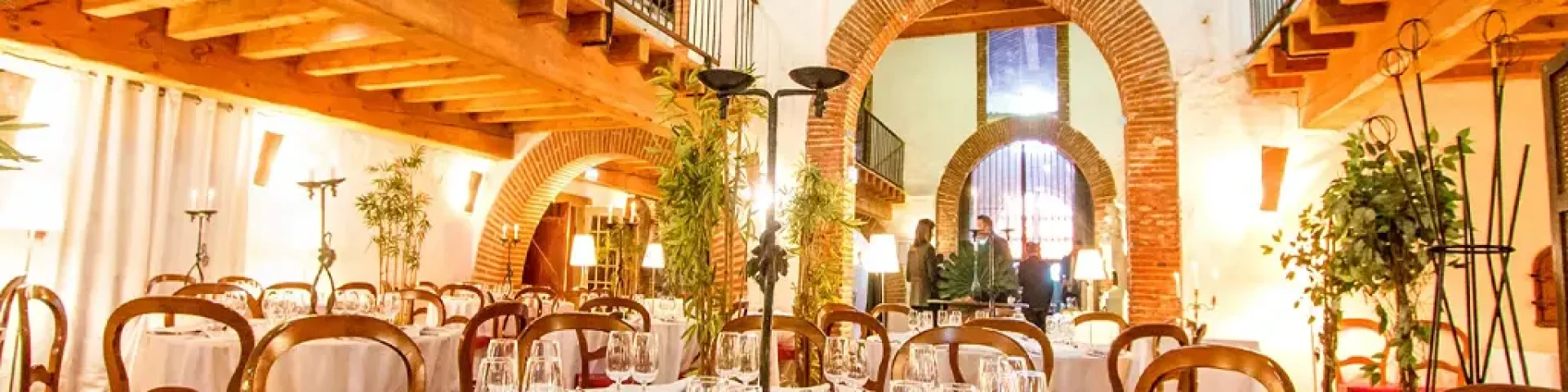 Grande salle voûtée aménagée pour un repas, avec tables dressées, chaises en bois et lumière chaleureuse.