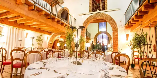 Grande salle voûtée aménagée pour un repas, avec tables dressées, chaises en bois et lumière chaleureuse.