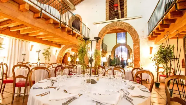 Grande salle voûtée aménagée pour un repas, avec tables dressées, chaises en bois et lumière chaleureuse.