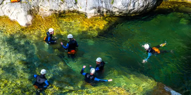 Groupe équipé de combinaisons et casques progressant dans un bassin d’eau claire au pied de rochers.