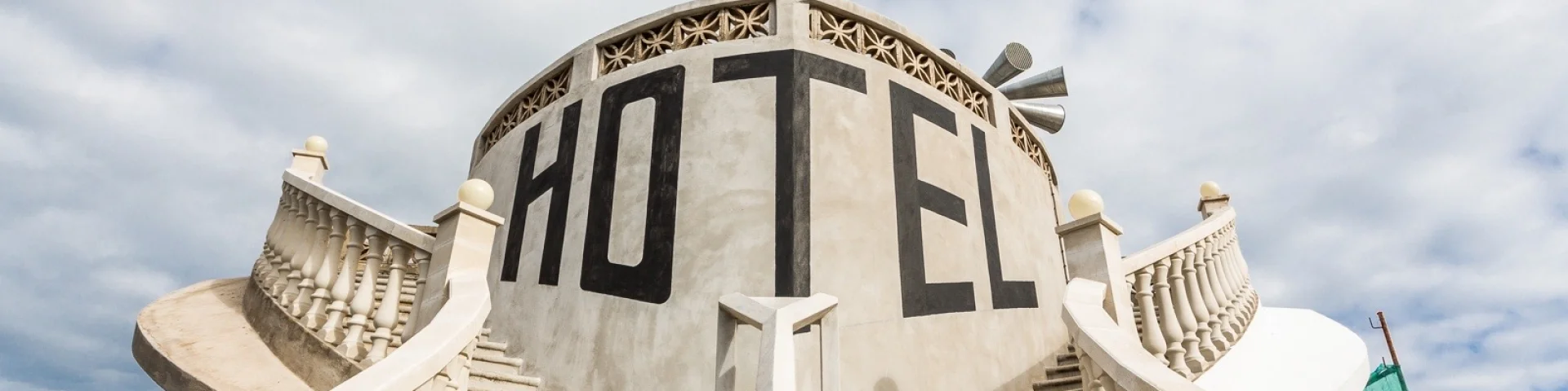 Escaliers symétriques menant à une façade circulaire portant l’inscription « Hôtel », sous un drapeau à rayures.