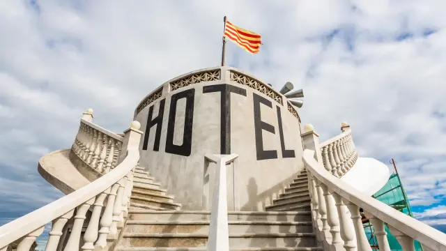Escaliers symétriques menant à une façade circulaire portant l’inscription « Hôtel », sous un drapeau à rayures.