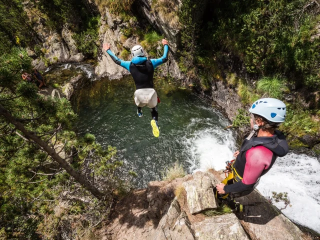 Personne en combinaison sautant d’un rocher dans un bassin naturel, un encadrant observant à côté.