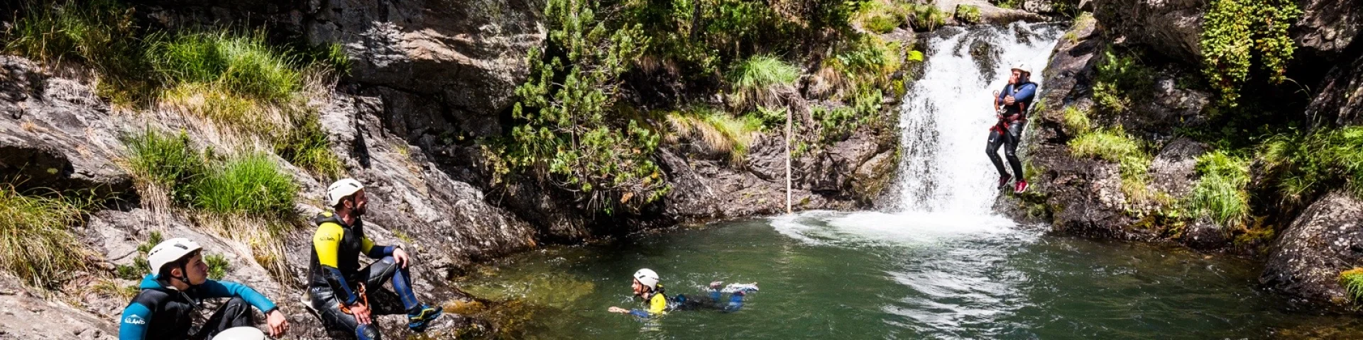 Participants en combinaison et casque évoluant dans un bassin naturel au pied d’une petite cascade.