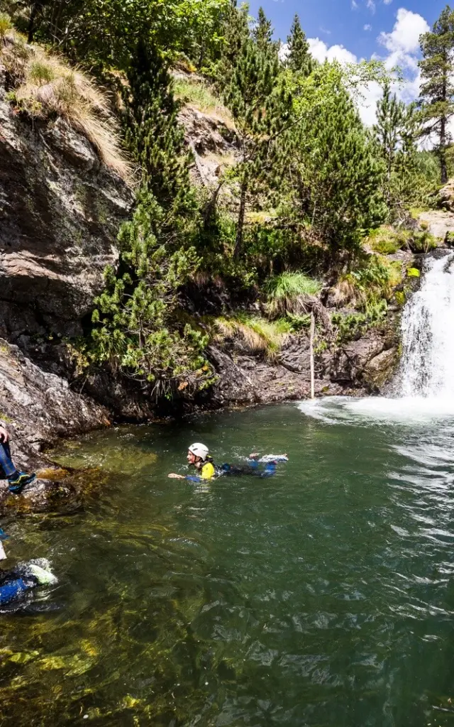 Participants en combinaison et casque évoluant dans un bassin naturel au pied d’une petite cascade.