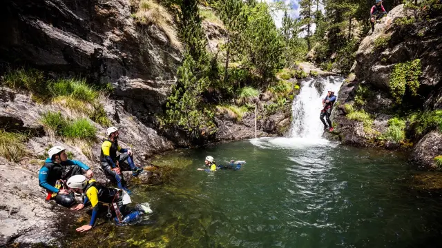 Participants en combinaison et casque évoluant dans un bassin naturel au pied d’une petite cascade.