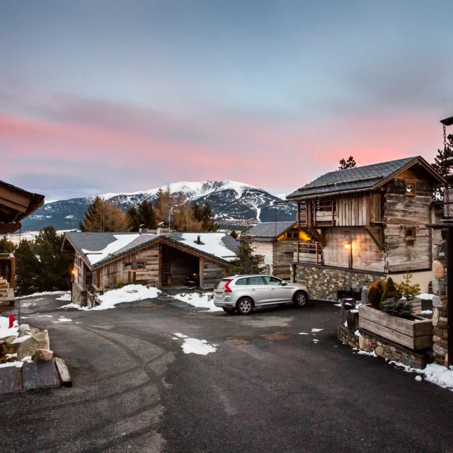 Vue en fin de journée sur les Chalets Secrets à Bolquère, avec un ciel rosé, des toits enneigés et les sommets du Canigó, du Gallinàs et du Cambre d’Aze en arrière-plan.