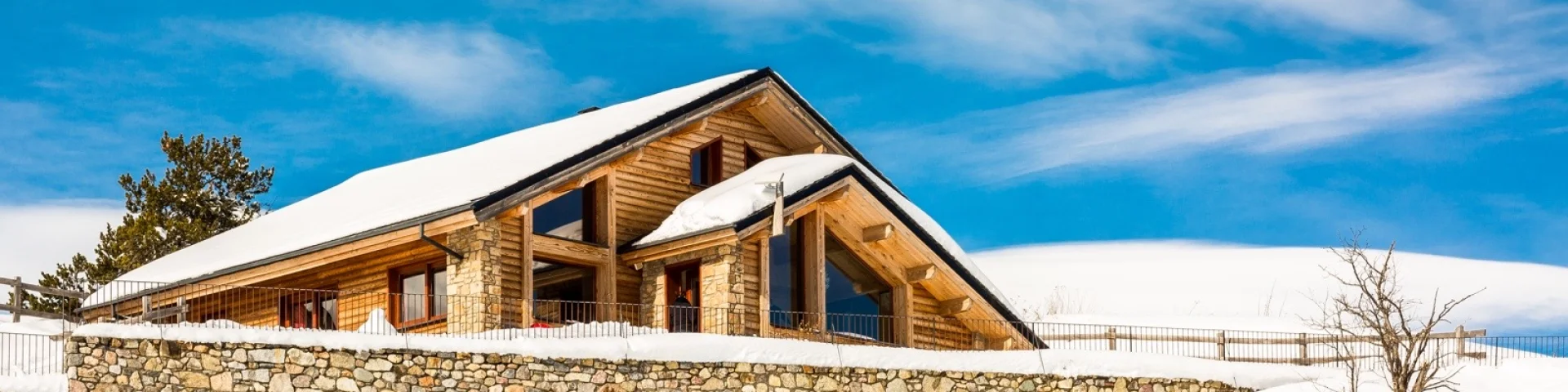Grand chalet en bois et pierre à Saint-Pierre-dels-Forcats, entouré de neige sous un ciel bleu lumineux.