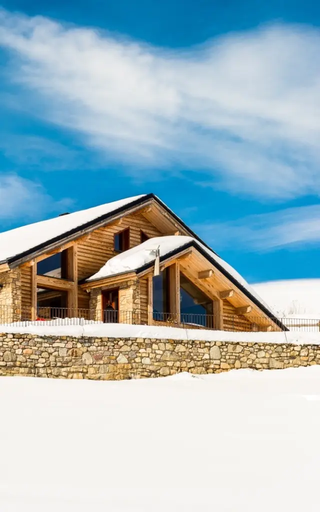 Grand chalet en bois et pierre à Saint-Pierre-dels-Forcats, entouré de neige sous un ciel bleu lumineux.