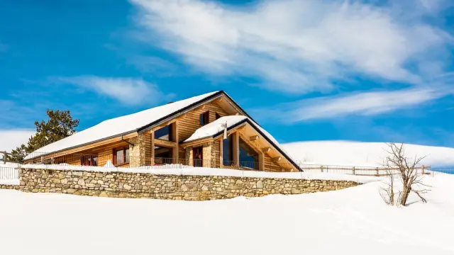 Grand chalet en bois et pierre à Saint-Pierre-dels-Forcats, entouré de neige sous un ciel bleu lumineux.