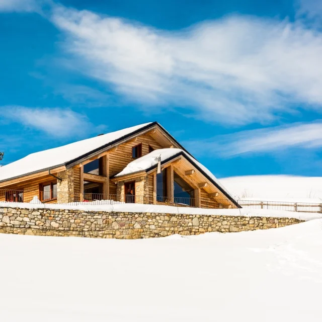 Grand chalet en bois et pierre à Saint-Pierre-dels-Forcats, entouré de neige sous un ciel bleu lumineux.