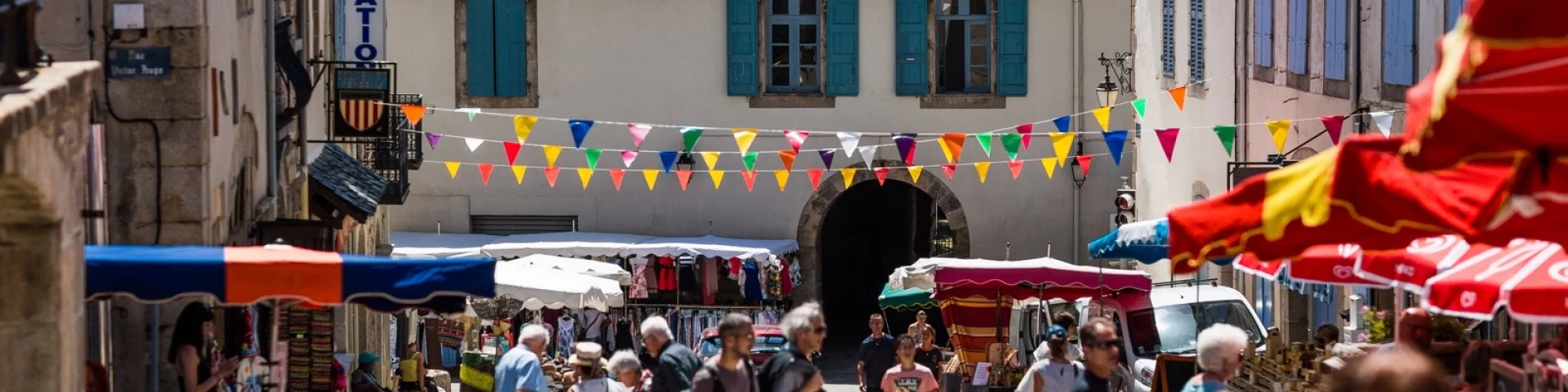 Marché en plein air dans une rue, avec stands colorés, passants et bâtiments anciens de la cité fortifiée.