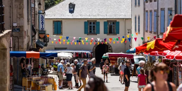 Marché en plein air dans une rue, avec stands colorés, passants et bâtiments anciens de la cité fortifiée.