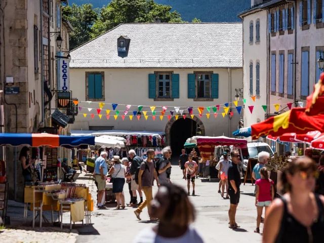 Marché en plein air dans une rue, avec stands colorés, passants et bâtiments anciens de la cité fortifiée.