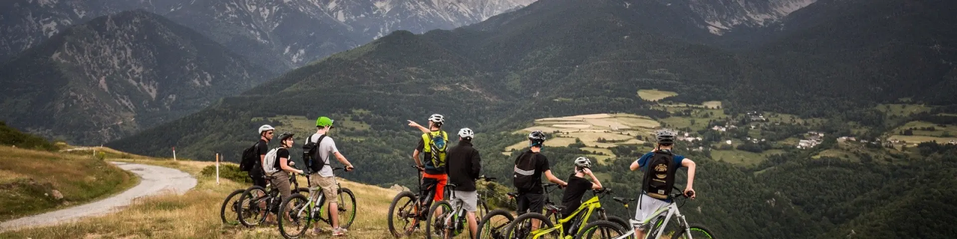 Groupe de cyclistes à VTT électrique arrêtés sur un plateau herbeux, observant un vaste panorama de montagnes et de vallées.