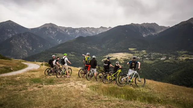 Groupe de cyclistes à VTT électrique arrêtés sur un plateau herbeux, observant un vaste panorama de montagnes et de vallées.